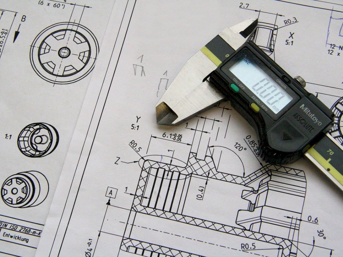 The image shows technical engineering drawings with a digital caliper placed on top, commonly used for precise measurement of objects.